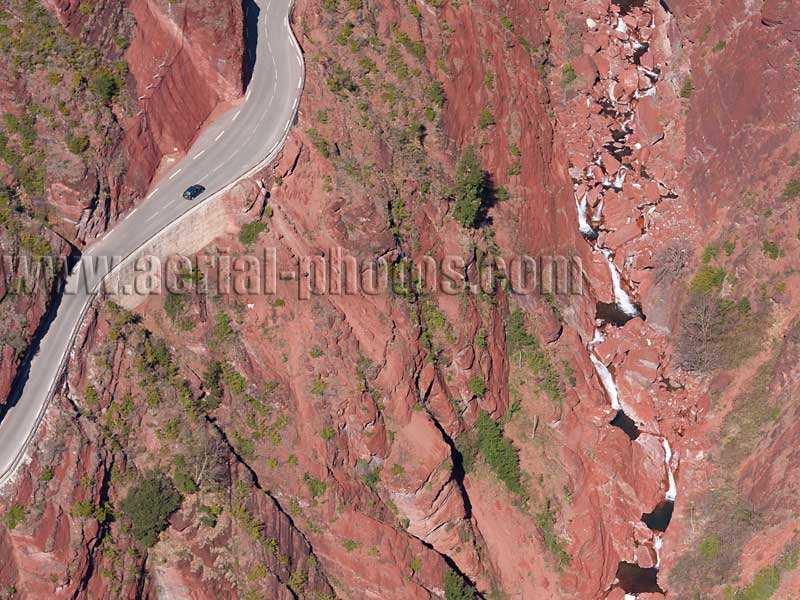 Aerial view of a scenic road inside a red canyon with waterfall in the Alps, France. Vue aérienne.