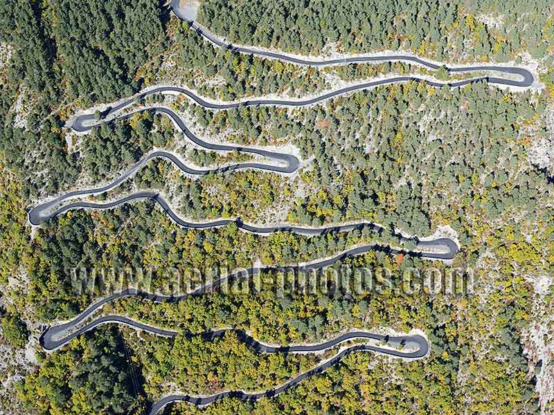 Aerial view of a road with switchbacks through a forest with fall colors in the French Alps. Vue aérienne.